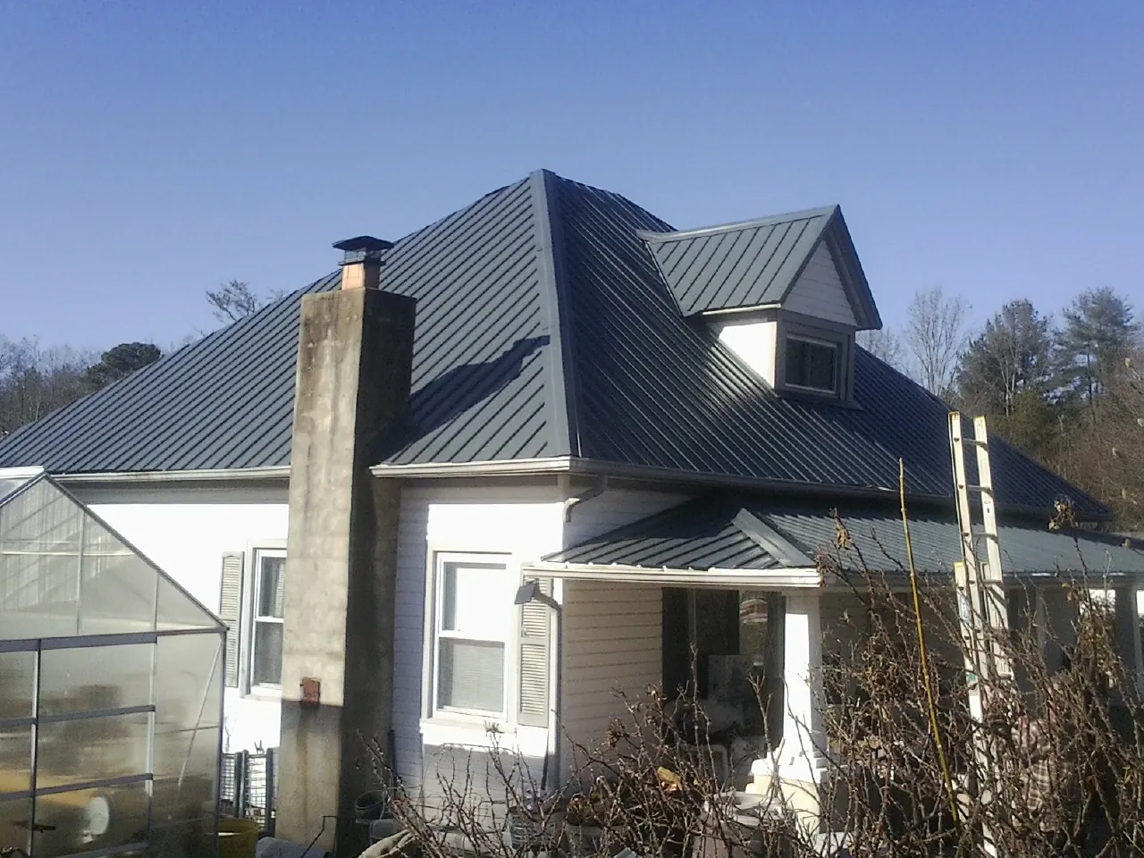 Dark blue standing seam metal roof on a white farmhouse with dormer — Slate & Tile Roof Repair by Roofing Brothers in Convent