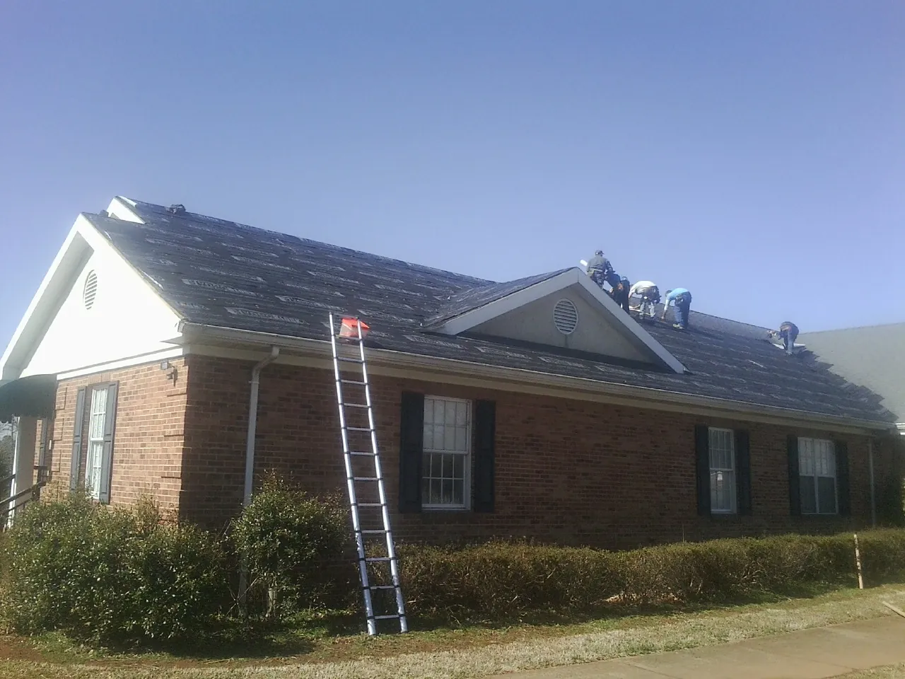 Crew tearing shingles off a brick ranch roof with a ladder set — Emergency Roof Repair work by our crew in Convent