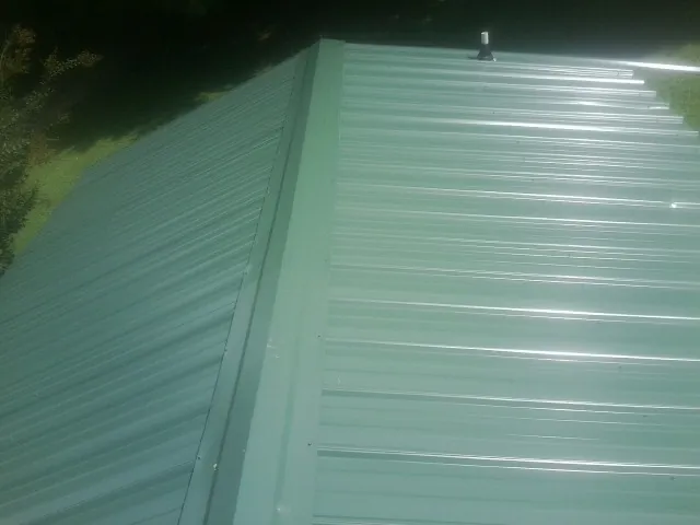 New green metal panels meeting at the ridge of a roof — Flat Roof Repair work by our crew in Convent