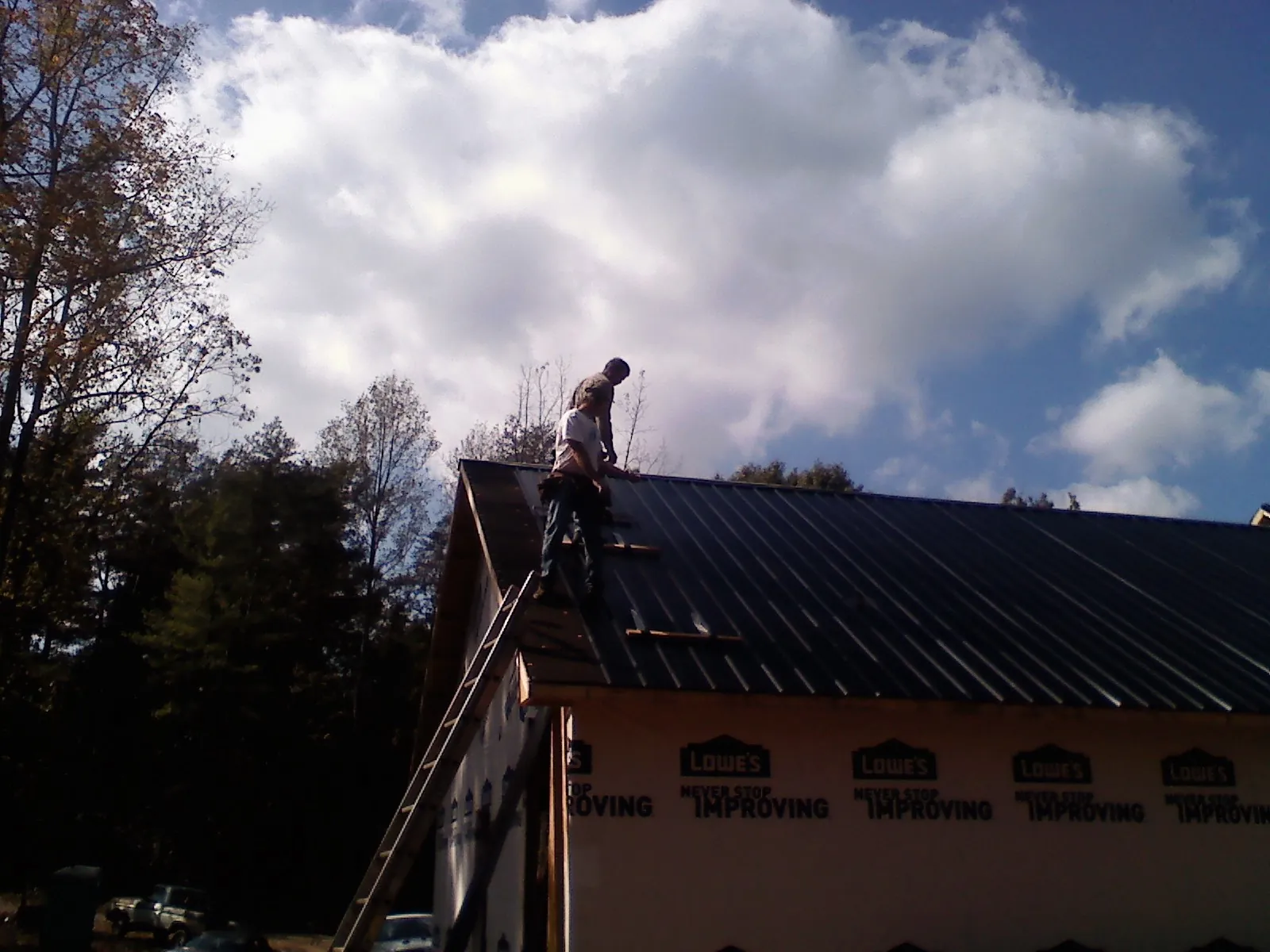 Roofer fastening dark metal panels high against a cloudy sky, from a Roof Inspection job in Convent