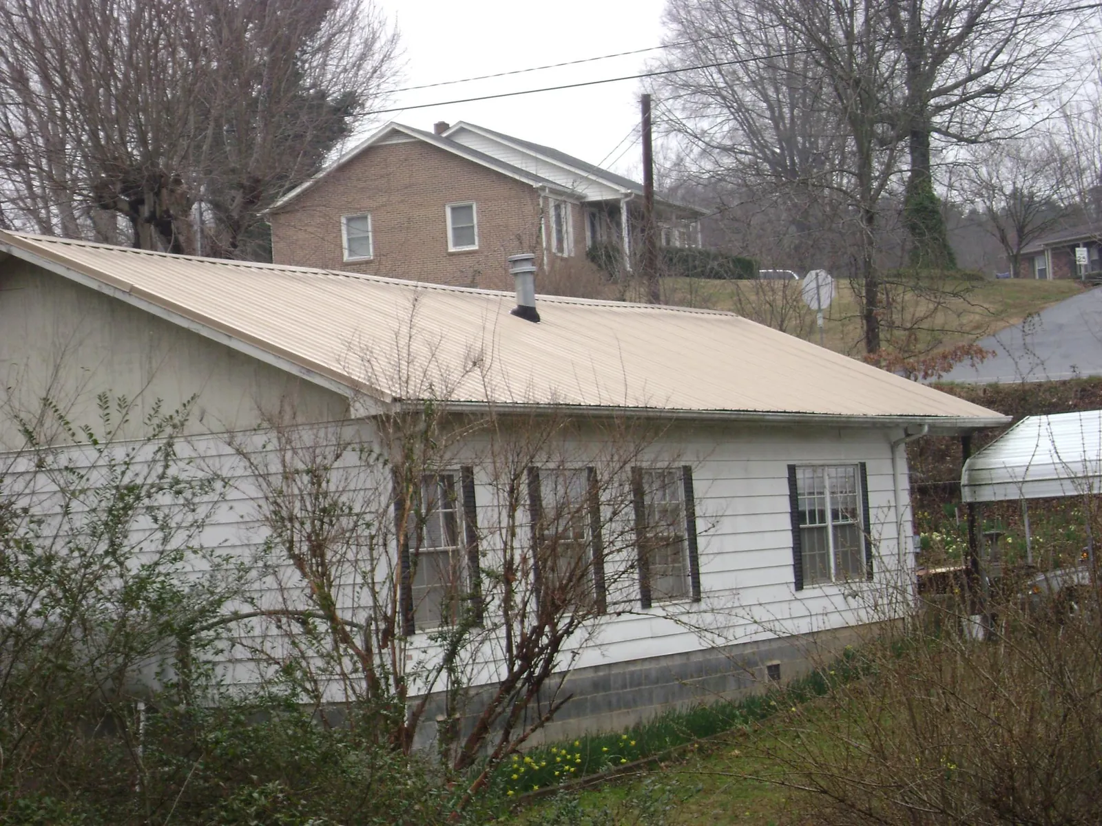 Tan metal roof on a white sided house set into a hillside — Commercial Roofing by Roofing Brothers in Convent