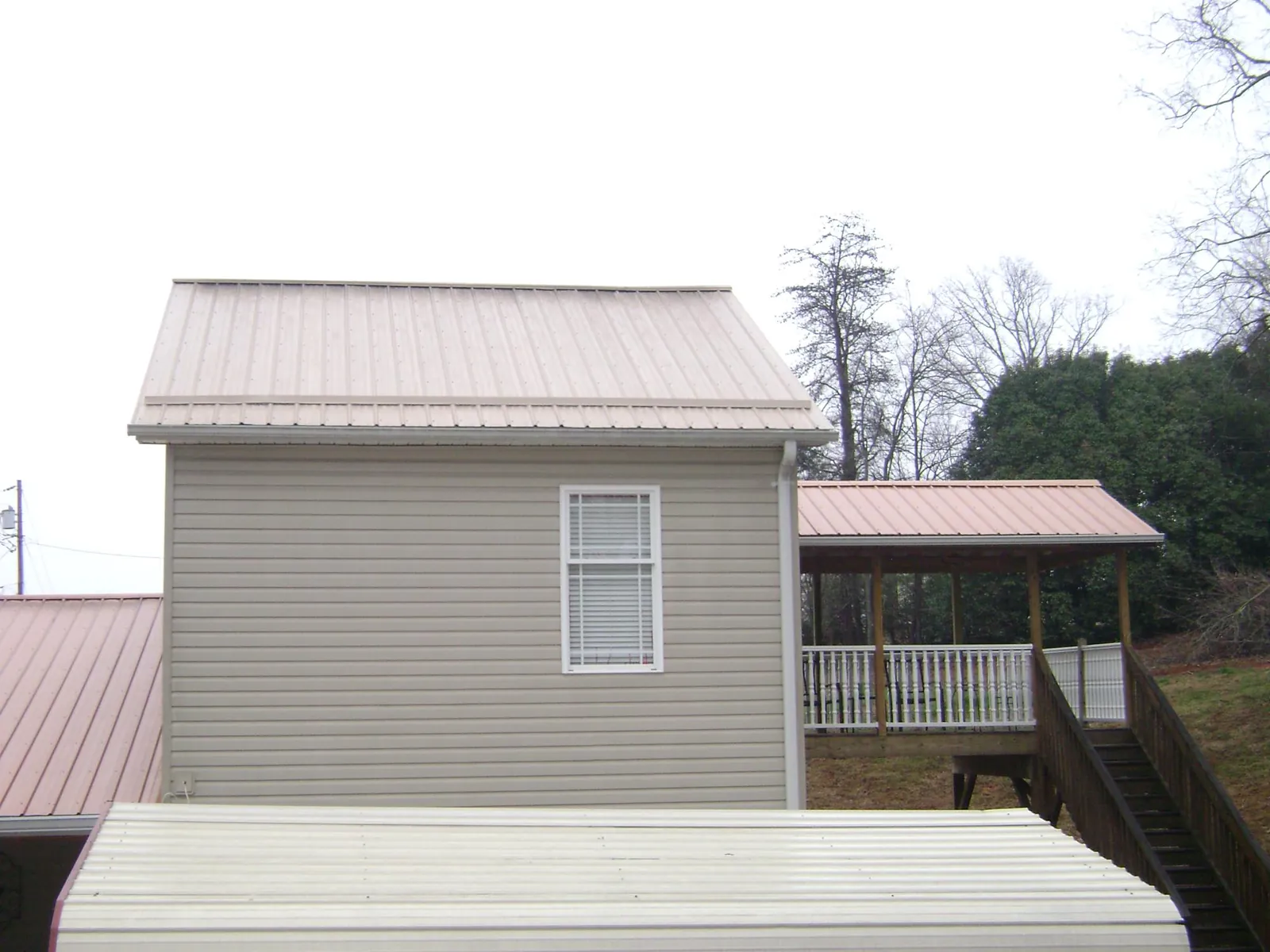 Tan metal roofs on a two story addition and attached porch, from a Roof Replacement job in Convent
